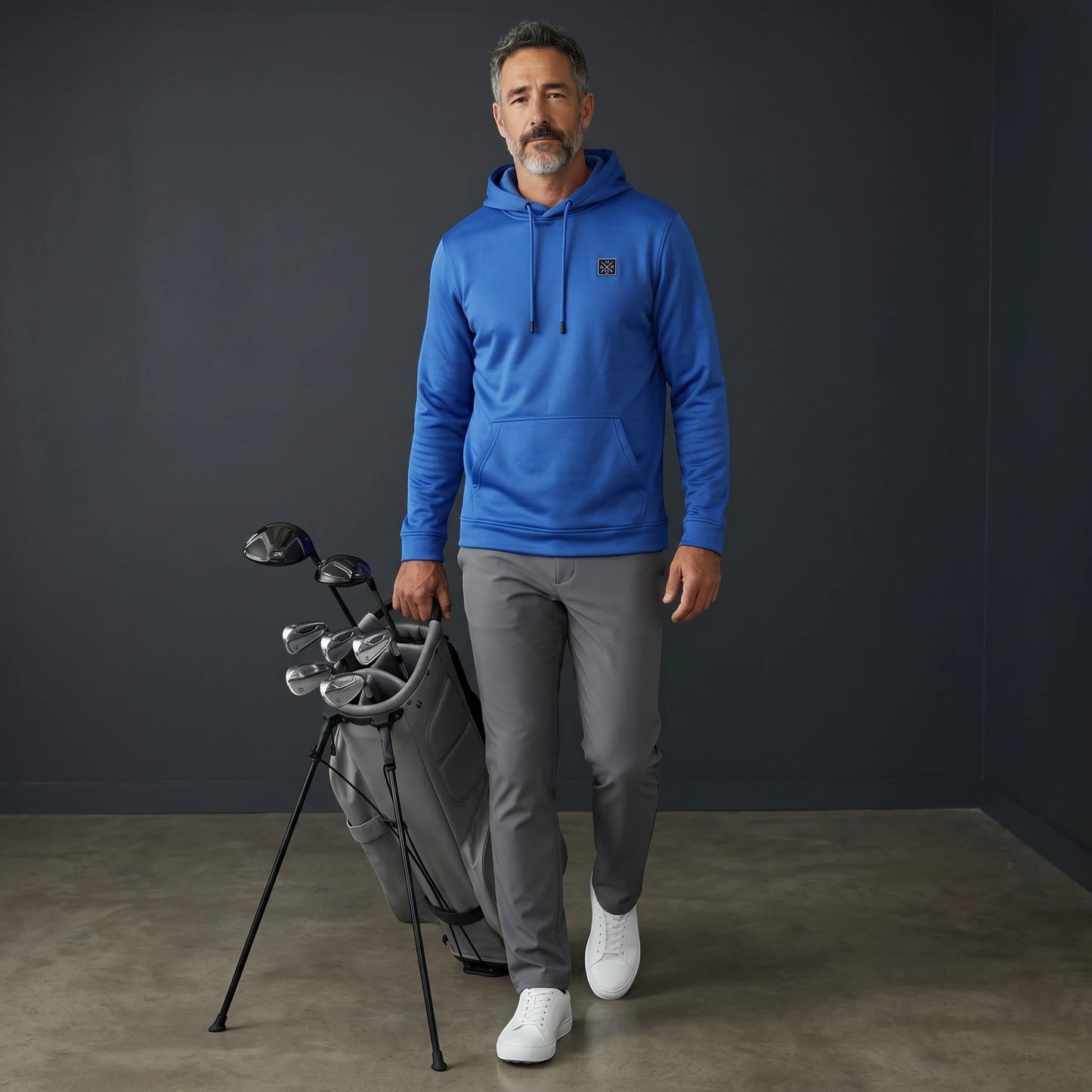 HARG royal blue performance fabric golf hoodie with kangaroo pocket and drawstring hood, worn by a man carrying a golf bag.